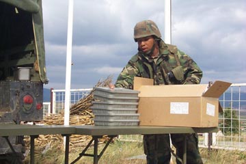 Sgt. Damian Sullivan stacks tray rations on a table while setting up the field mess